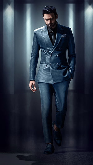 Prabhas in a sleek metallic blue double-breasted suit walking through a dramatic studio setting HD phone wallpaper