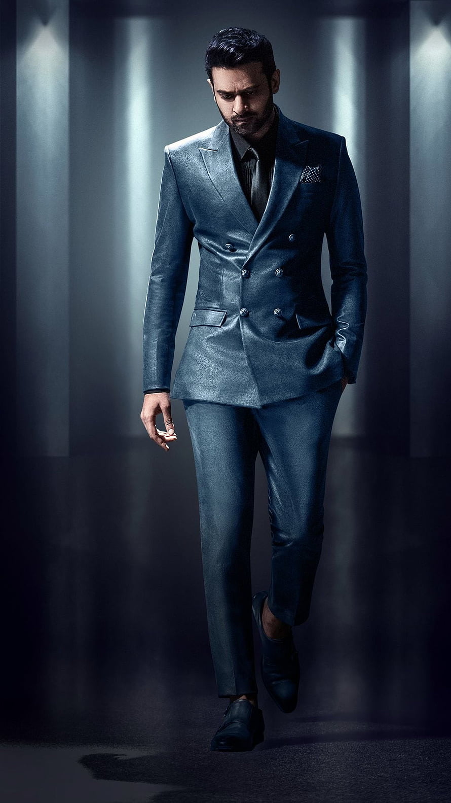 Prabhas in a sleek metallic blue double-breasted suit walking through a dramatic studio setting HD phone wallpaper