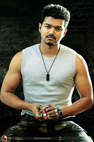 Vijay in Thuppakki Holding a Rubik's Cube Against a Dark Calligraphy Background HD phone wallpaper