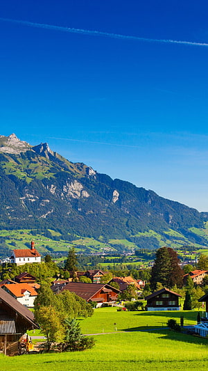 Scenic Swiss Alps Village with Green Meadows and Traditional Chalets HD phone wallpaper