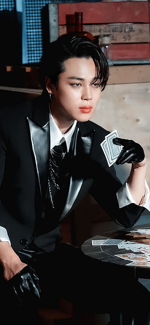 Jimin from BTS in a black suit and leather gloves holding playing cards at a table HD phone wallpaper