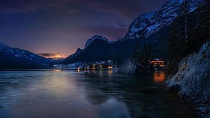Alpine Lake at Dusk with Snow-Capped Mountains and Glowing Village Lights HD wallpaper