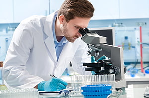 Scientist in White Lab Coat Examining Sample Under Microscope in Modern Laboratory HD wallpaper