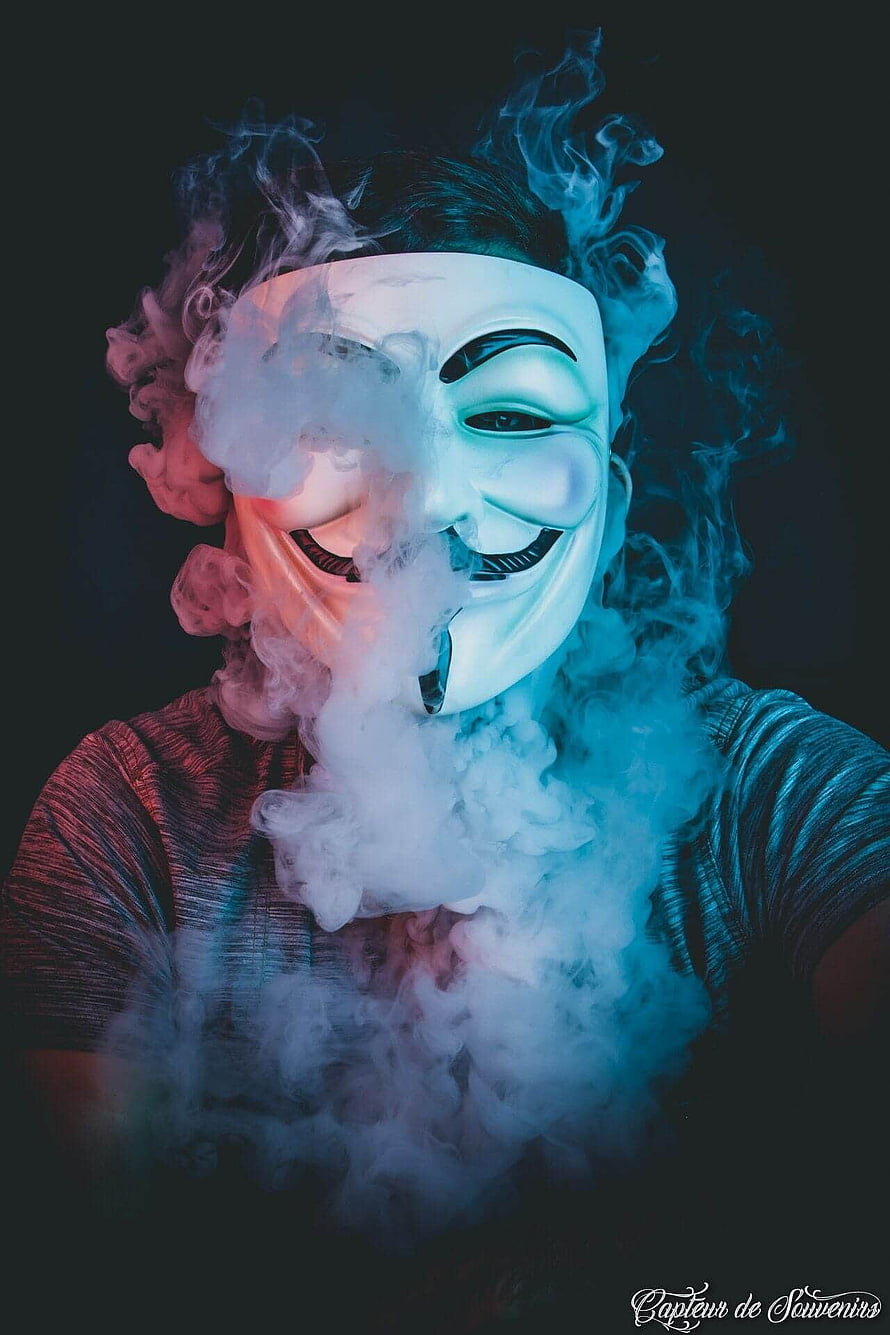 Person Wearing Guy Fawkes Mask Surrounded by Dramatic Smoke and Neon Lighting HD phone wallpaper