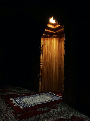 Illuminated wooden mihrab niche with prayer rug in dark mosque interior HD phone wallpaper