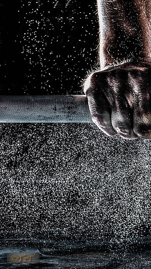 Close-up of a muscular hand gripping a barbell with water droplets splashing against a dark background HD phone wallpaper