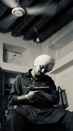 Diljit Dosanjh in a black shirt and white turban holding a pistol in a moody black and white portrait HD phone wallpaper