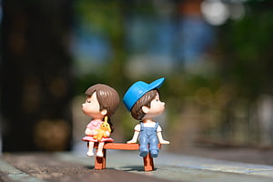 Cute Miniature Couple Dolls Sitting on a Tiny Bench with Soft Bokeh Background HD wallpaper
