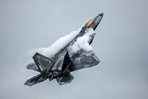 F-22 Raptor Stealth Fighter Jet Breaking Through Clouds in High Speed Flight HD wallpaper