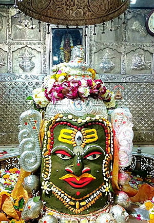 Sacred Shiva Lingam adorned with green sandalwood paste, vibrant floral garlands, and silver cobra sculptures in a temple shrine HD phone wallpaper