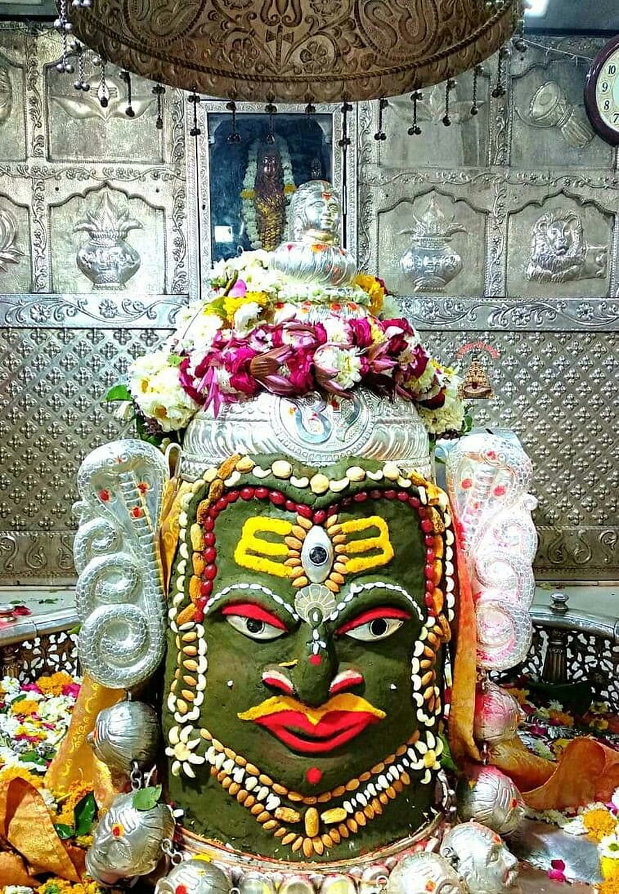 Sacred Shiva Lingam adorned with green sandalwood paste, vibrant floral garlands, and silver cobra sculptures in a temple shrine HD phone wallpaper