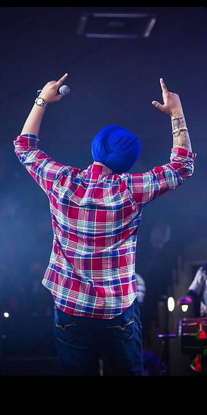 Diljit Dosanjh performing on stage wearing a blue turban and red plaid shirt HD phone wallpaper