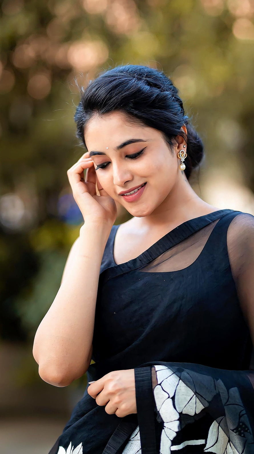 Portrait of a woman in a black saree with floral print, smiling gently with hand near face, soft bokeh background, Priyanka mohan, telugu actress, saree beauty HD phone wallpaper