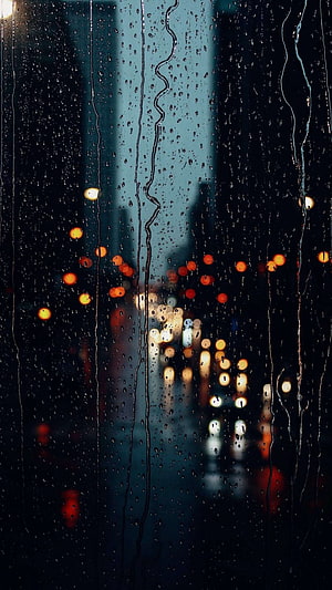 Raindrops on a window pane with blurred city lights glowing through the glass at night HD phone wallpaper