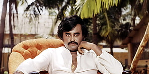 Rajinikanth in white shirt seated outdoors with palm trees in background HD wallpaper
