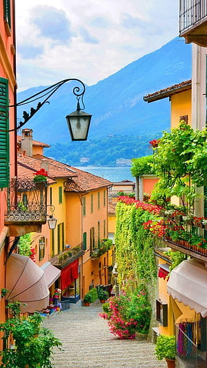Charming Cobblestone Street in Bellagio, Lake Como, Italy with Vibrant Flowers and Mountain Views HD phone wallpaper