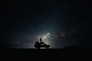 Silhouette of a person standing on an off-road vehicle under the Milky Way galaxy night sky HD wallpaper