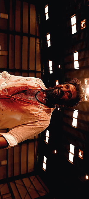 Pawan Kalyan in a blood-stained white shirt with a menacing grin in a dark industrial setting HD phone wallpaper