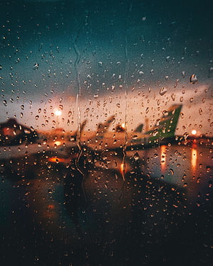 Rainy Airport Window View at Sunset with Blurred Terminal Lights and Water Droplets HD phone wallpaper