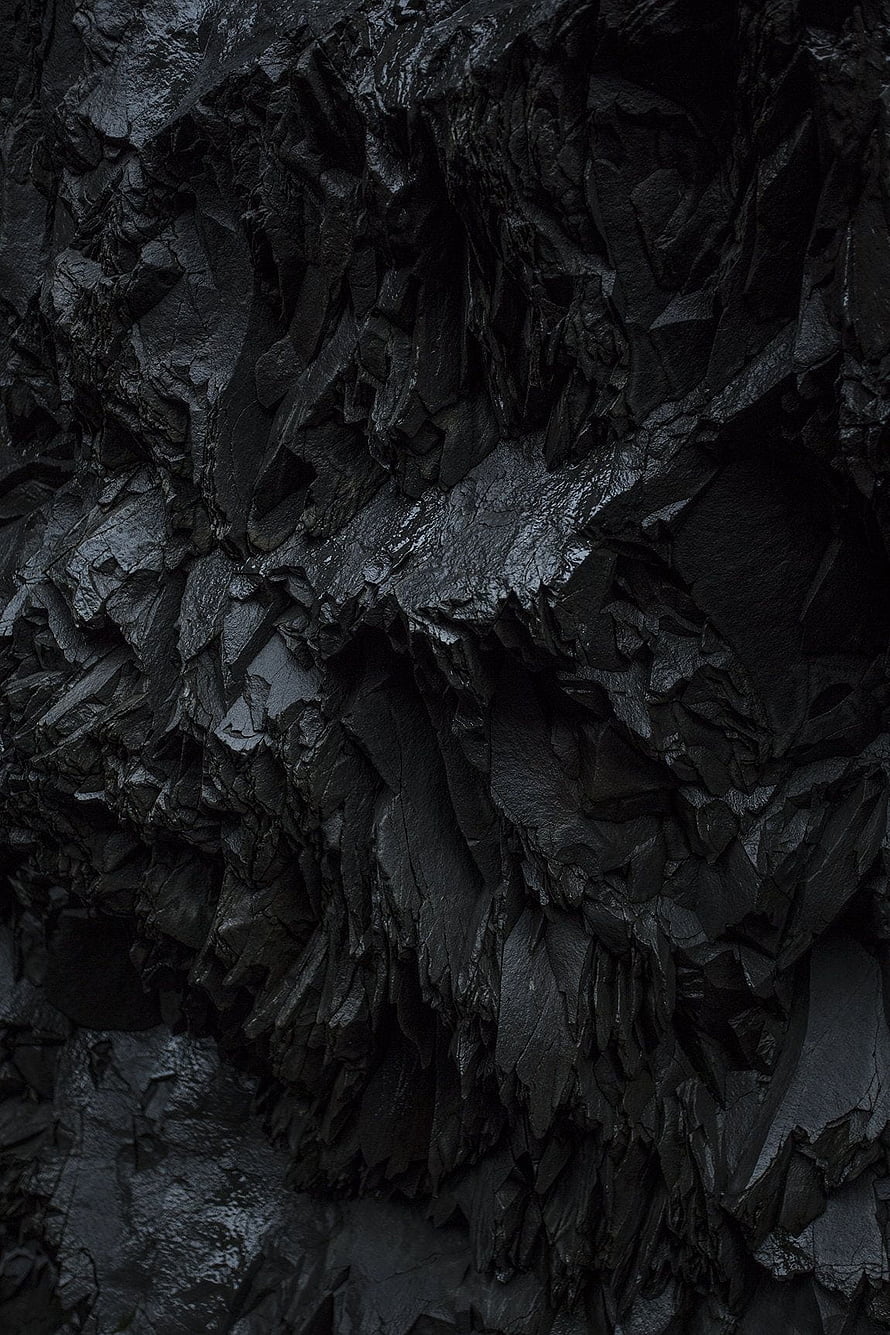 Dark volcanic rock texture with glossy black mineral surfaces and rugged natural formations HD phone wallpaper