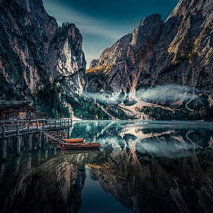 Serene Alpine Lake with Wooden Boats and Pier Surrounded by Dramatic Mountain Peaks HD phone wallpaper