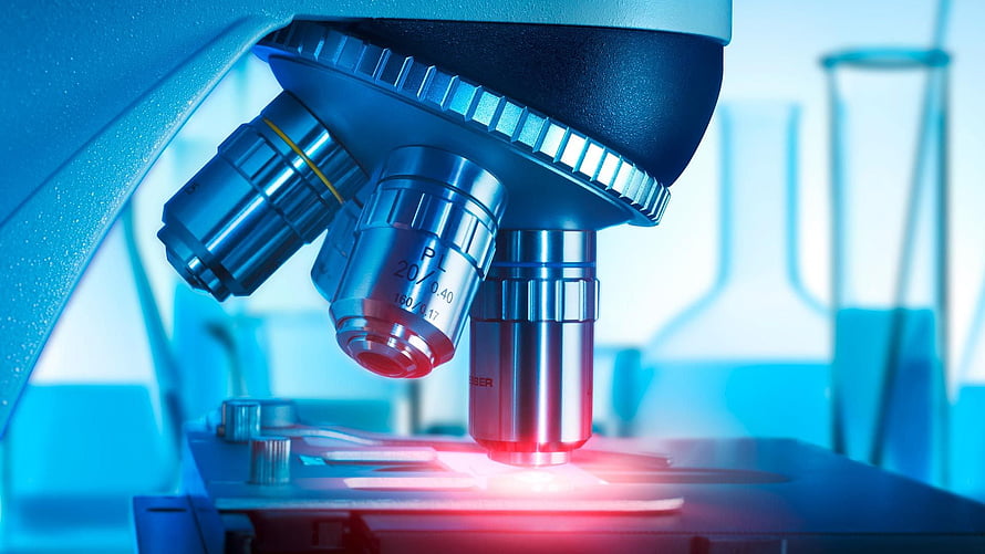 Close-up of a laboratory microscope with objective lenses and glowing specimen stage in a medical research setting HD wallpaper