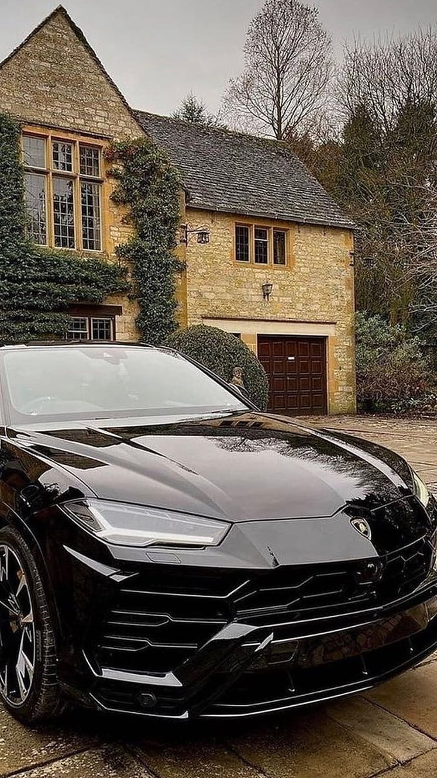 Black Lamborghini Urus SUV Parked in Front of a Traditional English Stone Cottage HD phone wallpaper