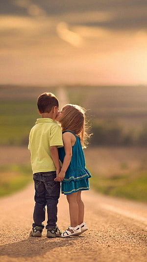 Two young children standing on a country road at golden hour with a warm sunset sky HD phone wallpaper