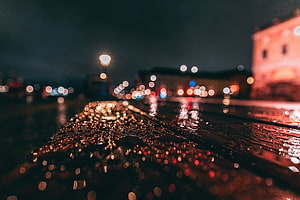Rain-soaked asphalt at night with glowing bokeh lights and water droplets HD wallpaper