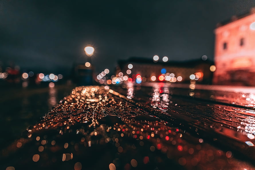 Rain-soaked asphalt at night with glowing bokeh lights and water droplets HD wallpaper