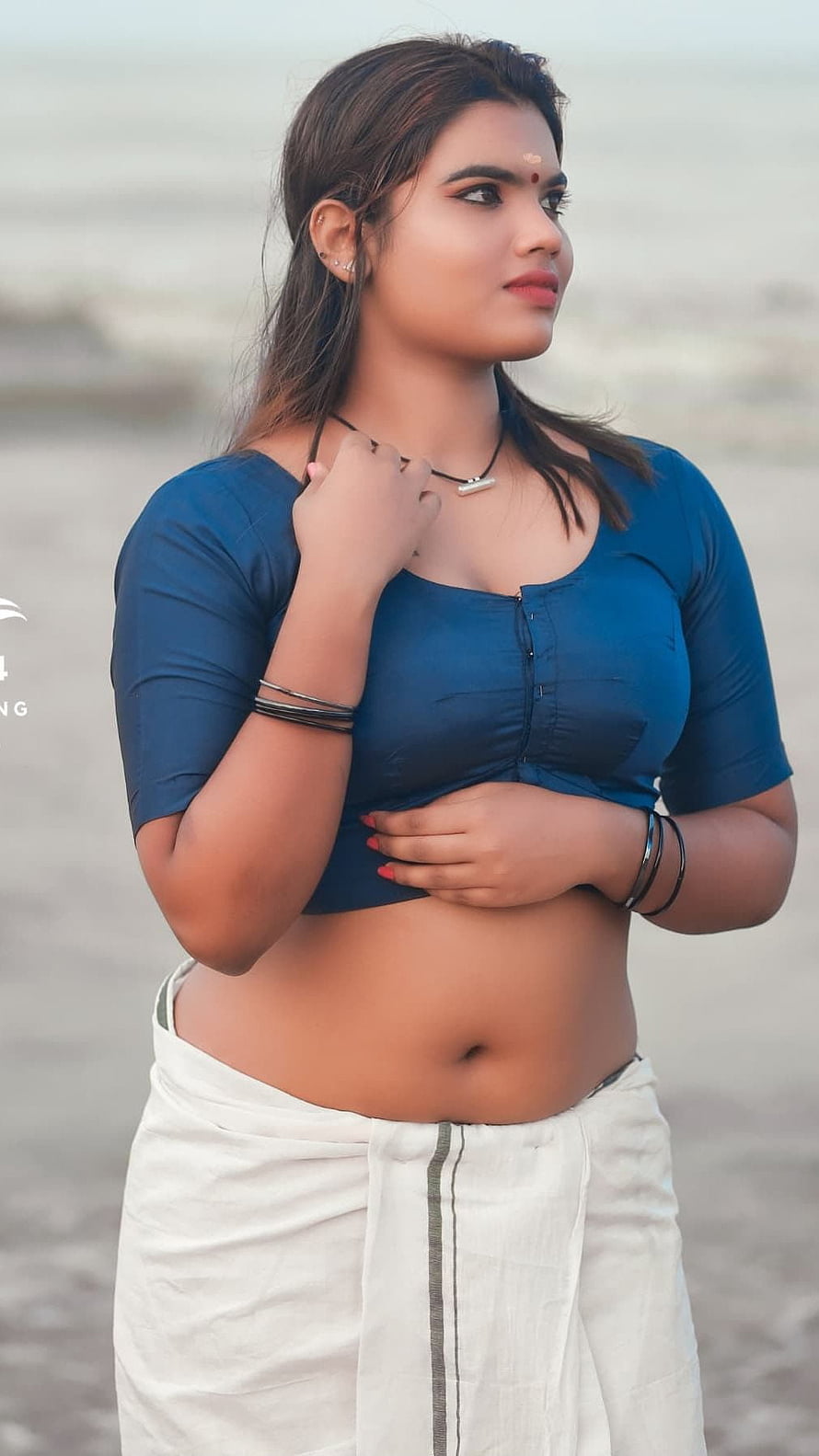 Aparna Nair in a blue crop top and white dhoti on a sandy beach HD phone wallpaper