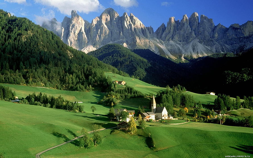 Alpine Village with Church Nestled in Green Meadows Beneath Dramatic Dolomite Peaks HD wallpaper