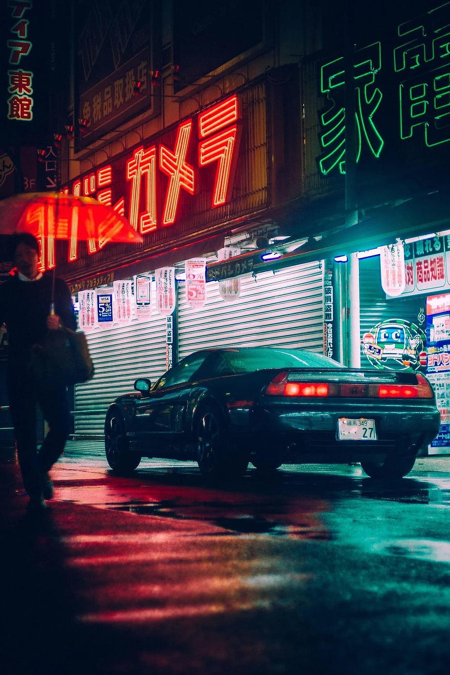 Honda NSX parked on a rainy Tokyo street at night with neon signs and a pedestrian with an umbrella HD phone wallpaper