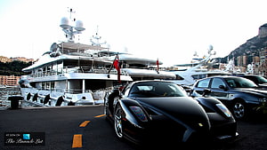 Black Ferrari Enzo parked at Monaco harbor with luxury yachts in background HD wallpaper