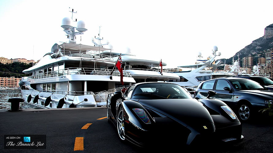 Black Ferrari Enzo parked at Monaco harbor with luxury yachts in background HD wallpaper