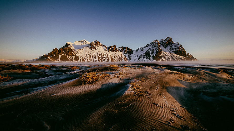 Snow-Capped Mountain Range Rising Above a Vast Frozen Tundra at Golden Hour HD wallpaper