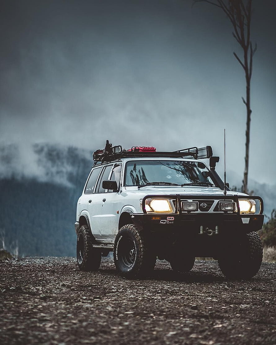 White Nissan Patrol off-road SUV with roof rack and bull bar on a gravel mountain overlook HD phone wallpaper