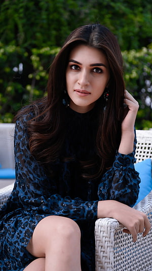 Kriti Sanon in a dark blue sequined dress seated on a white wicker chair outdoors HD phone wallpaper