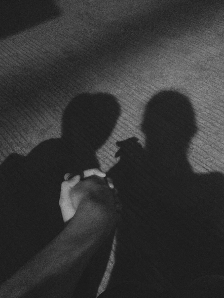 Black and white photo of two people holding hands with long shadows on a textured ground HD phone wallpaper