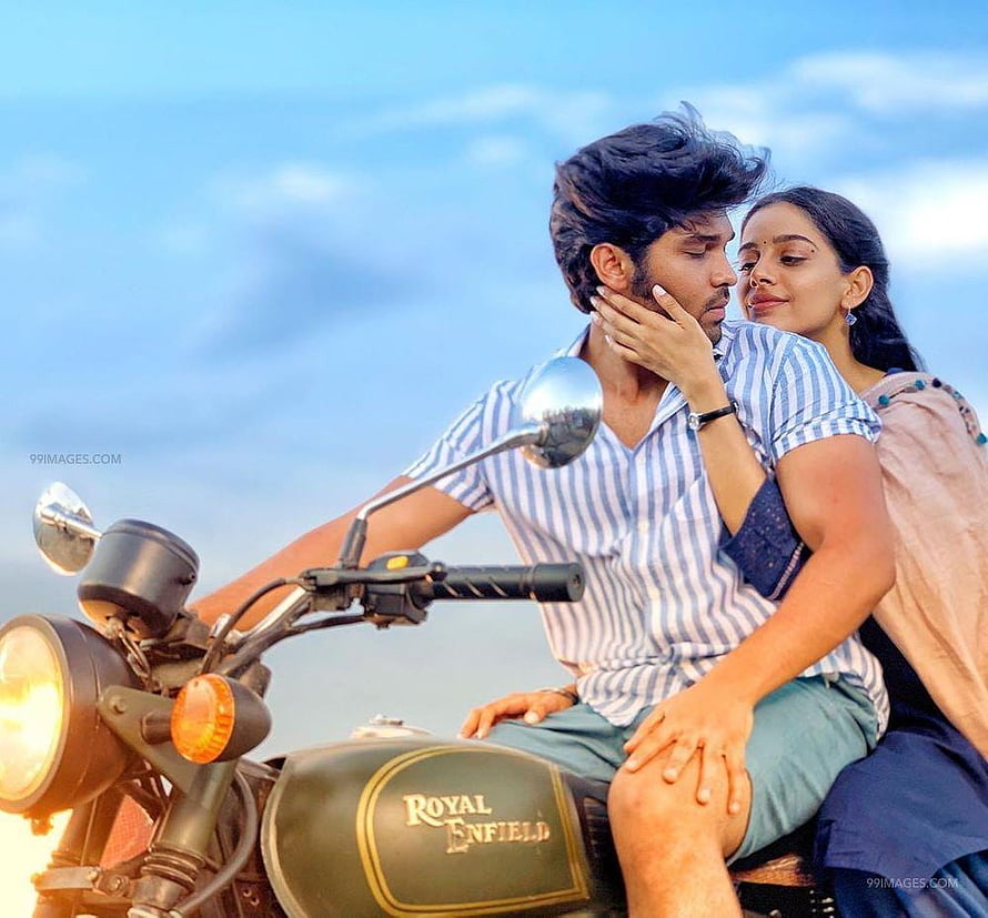 Adithya Varma and female co-star sharing a romantic moment on a Royal Enfield motorcycle HD wallpaper
