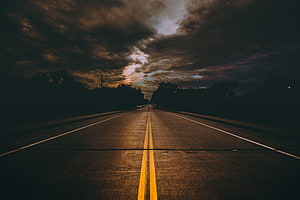 Moody Two-Lane Highway Stretching Into a Dramatic Overcast Sky at Dusk HD wallpaper