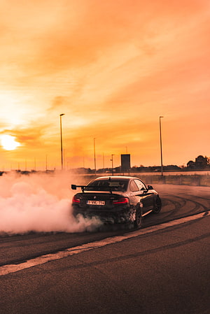 BMW M4 performing a drift on an open track at sunset with thick tire smoke HD phone wallpaper