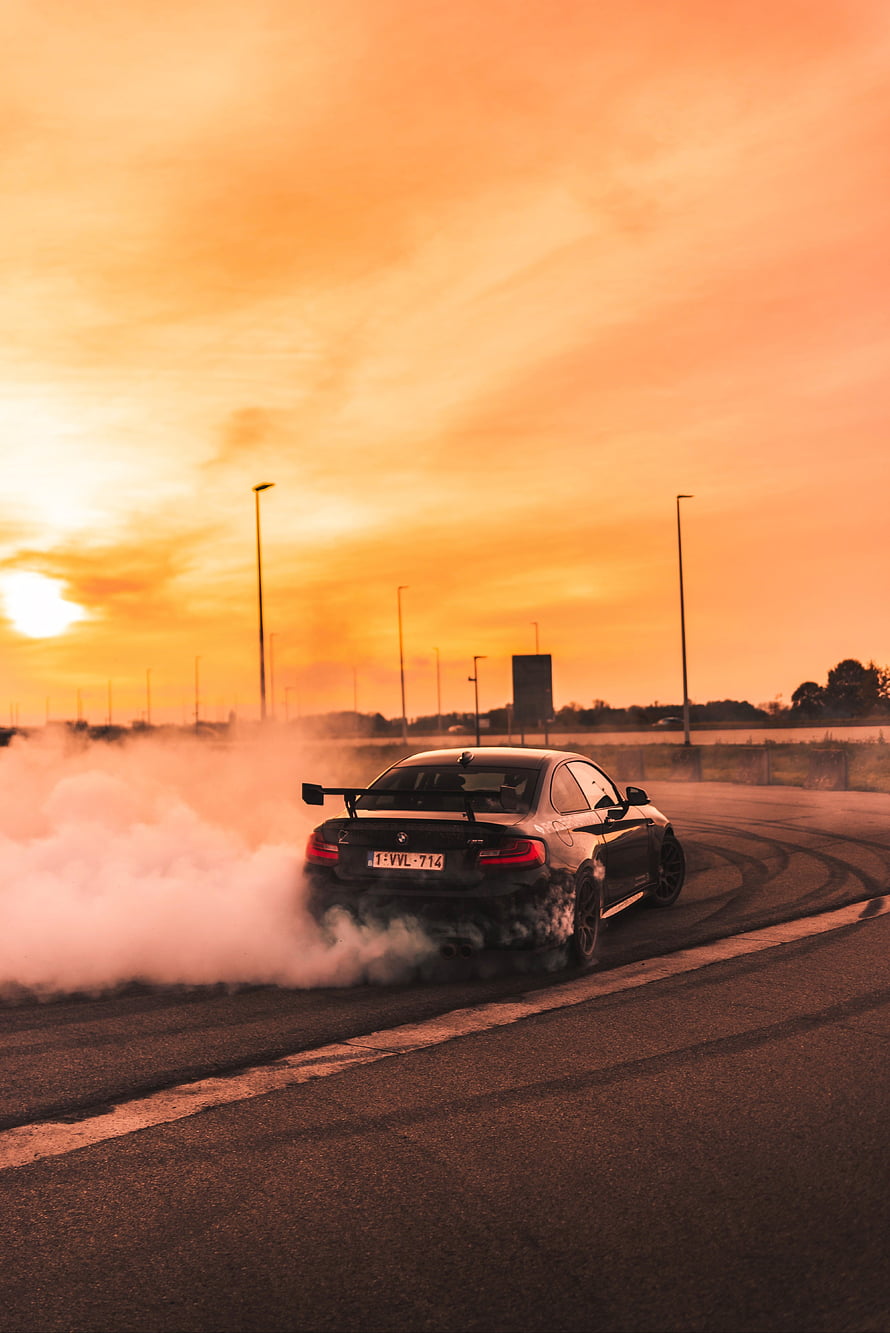 BMW M4 performing a drift on an open track at sunset with thick tire smoke HD phone wallpaper