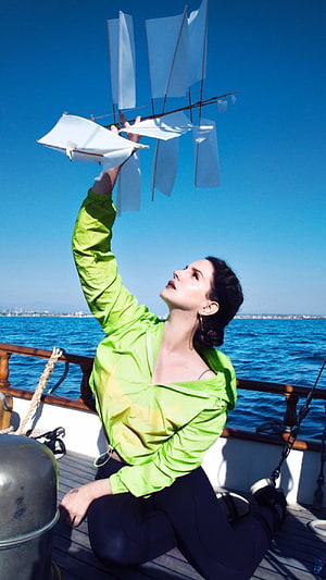 Lana Del Rey on a sailboat deck holding a model ship against a clear blue sky HD phone wallpaper