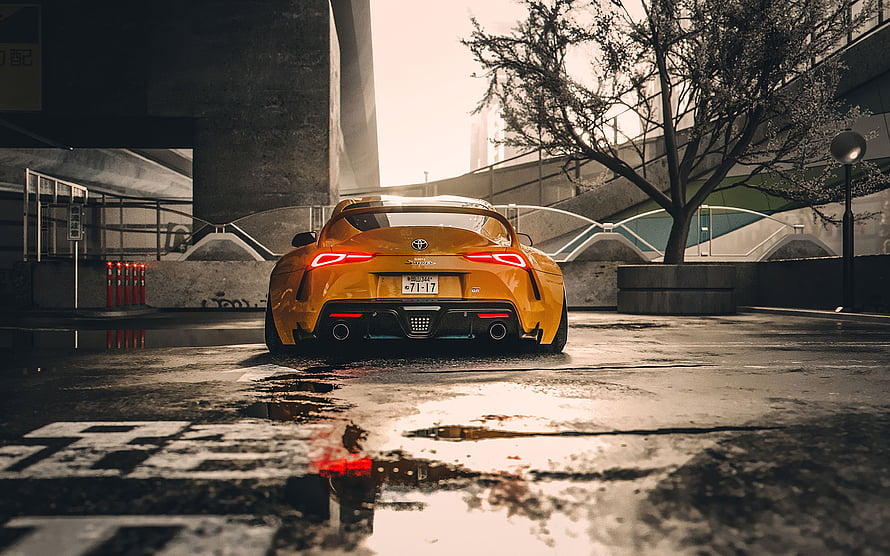 Rear View of a Yellow Toyota Supra Parked on a Wet Urban Street HD wallpaper