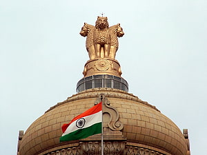 Golden Lion Capital of Ashoka atop the Indian Parliament House dome with the national flag waving against a clear sky HD wallpaper