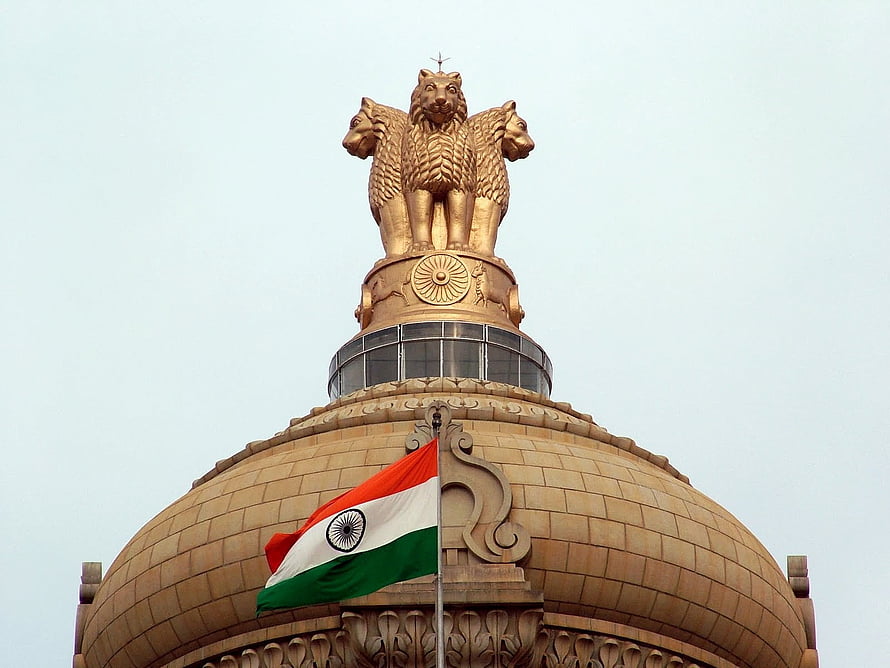 Golden Lion Capital of Ashoka atop the Indian Parliament House dome with the national flag waving against a clear sky HD wallpaper