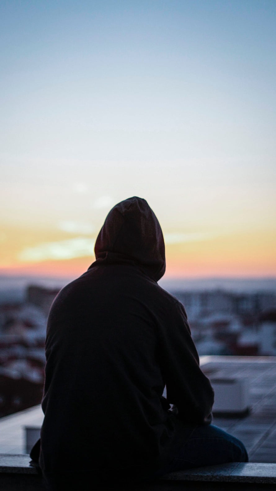 Silhouette of a Hooded Figure Sitting on a Rooftop at Sunset HD phone wallpaper