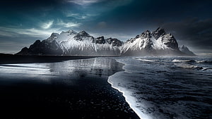 Dramatic Snow-Capped Mountains Rising Over a Dark Shoreline in Iceland HD wallpaper