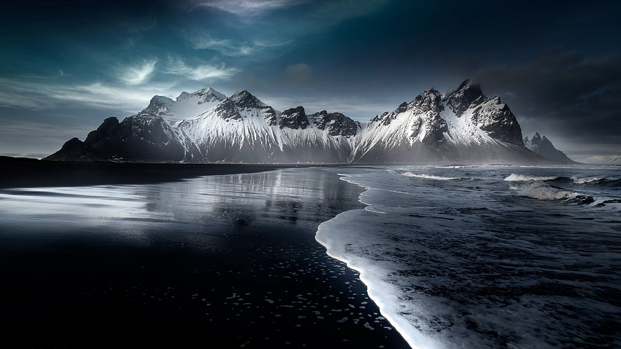 Dramatic Snow-Capped Mountains Rising Over a Dark Shoreline in Iceland HD wallpaper